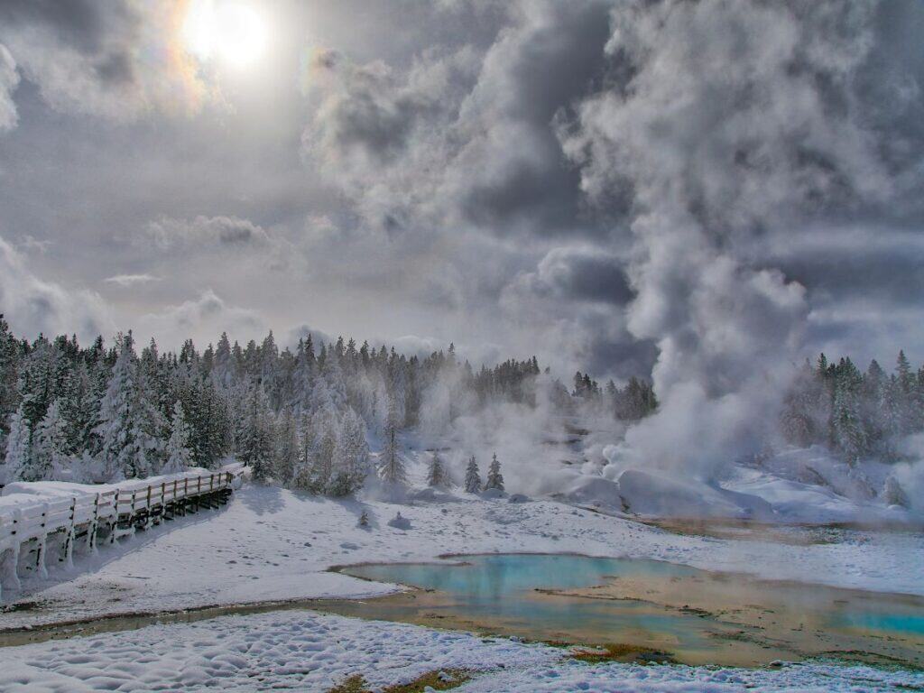 Steam rises from the ground in a snowy Norris Geyser Basin in winter