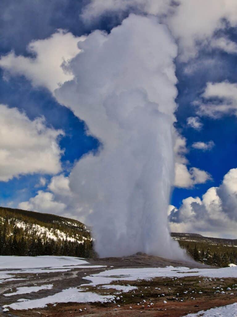 Old Faithful erupts into the sky as the ground is blanketed in snow