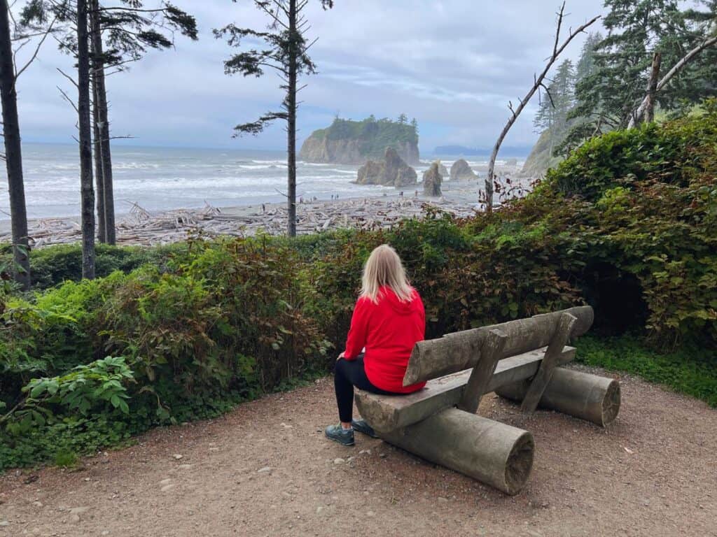 A woman sits on a bench, enjoying the view of Ruby Beach