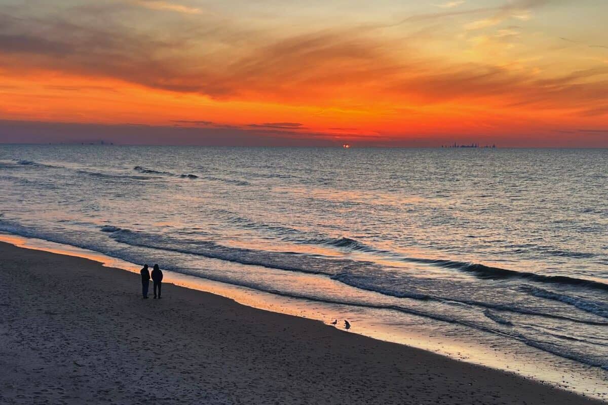 A man and woman watch sunset at a beach in Indiana Dunes National Park
