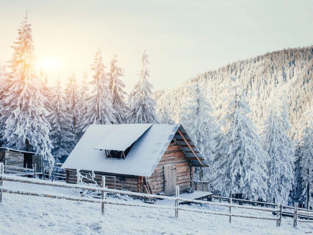 A cabin quietly sits in the snowy mountains as the sun rises on the horizon