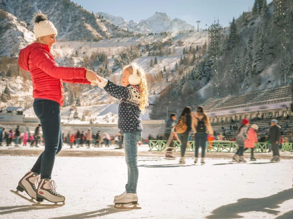 A mother and daughter enjoy outdoor ice skating with a view of mountains