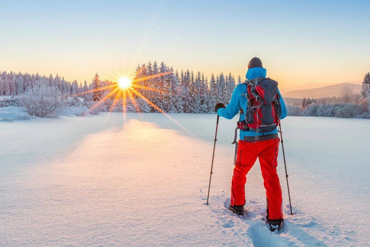A person walks in snowshoes toward the rising sun.