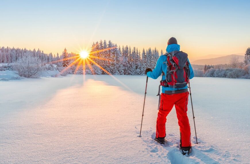 A person walks in snowshoes toward the rising sun.
