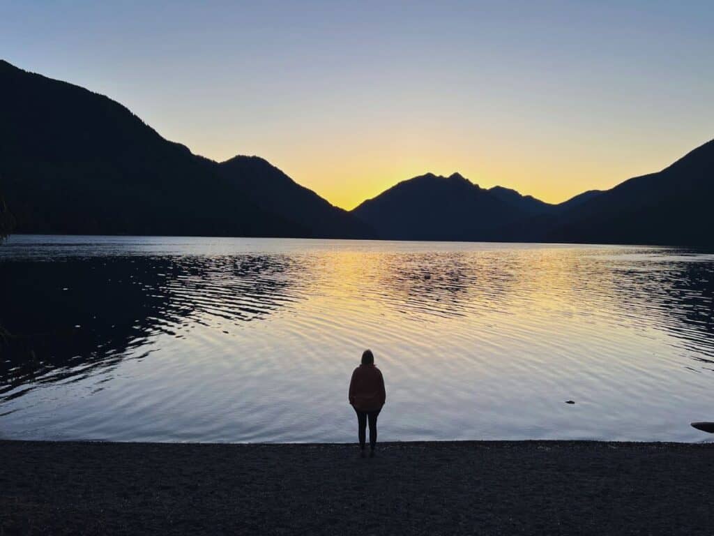 A woman watches sunrise across Lake Crescent, Olympic National Park, WA.