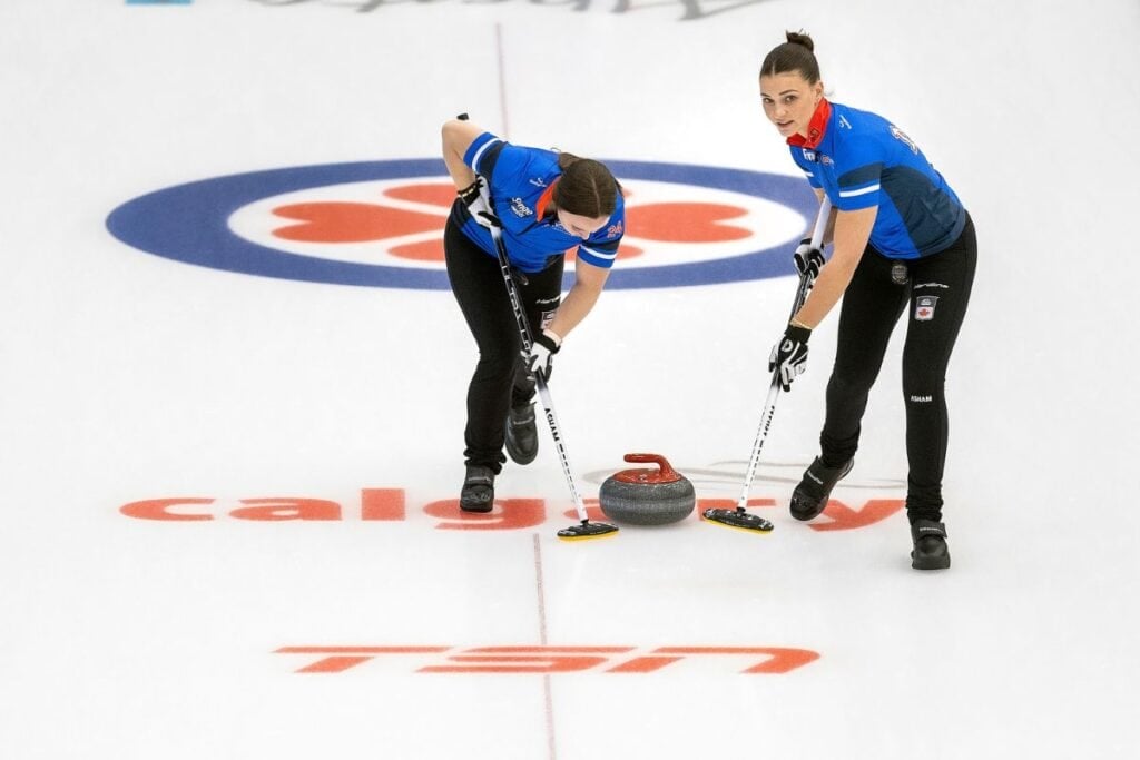 Two women sweep the ice in front of a curling stone during a match.