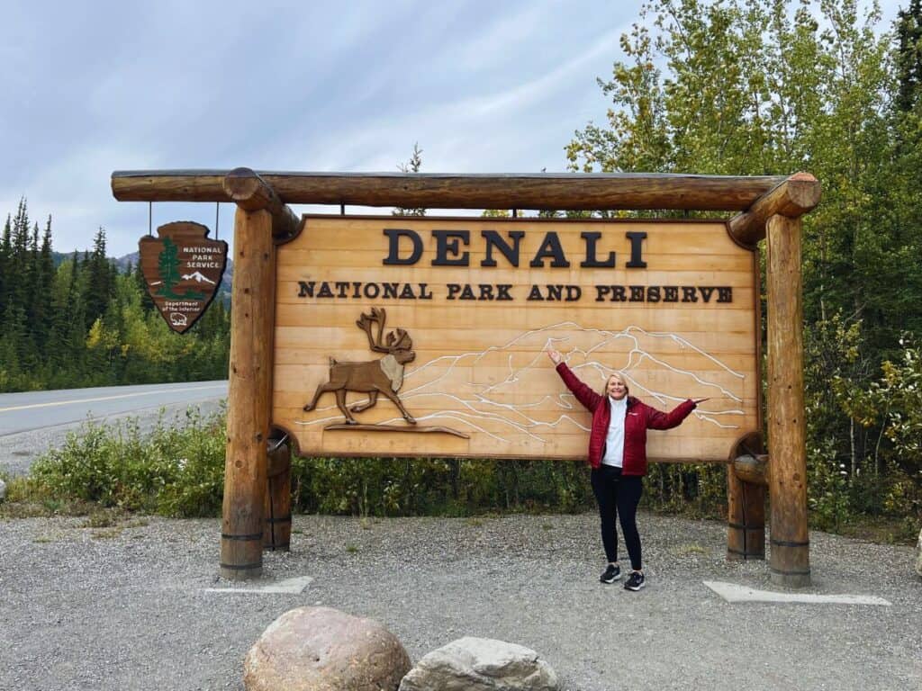 A woman poses in front of the Denali National Park sign.