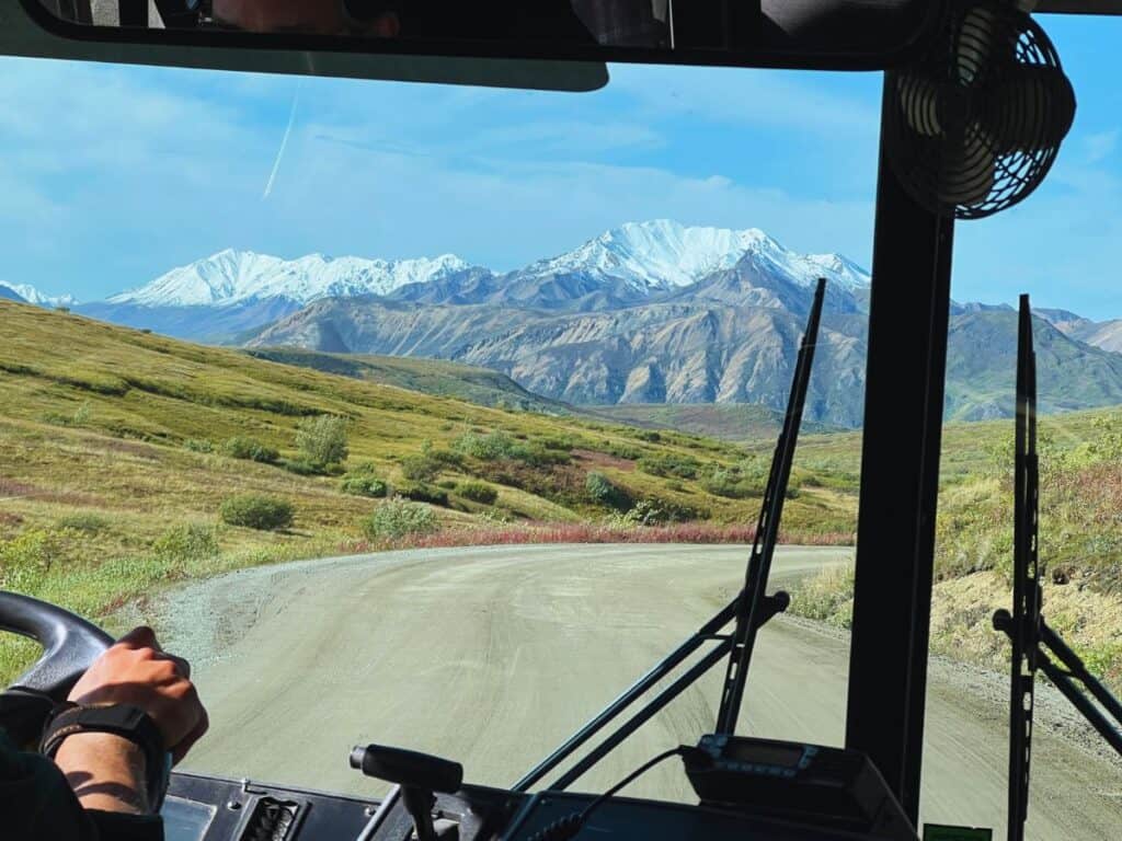 View of snowy mountains through the windshield of a Denali transit bus.