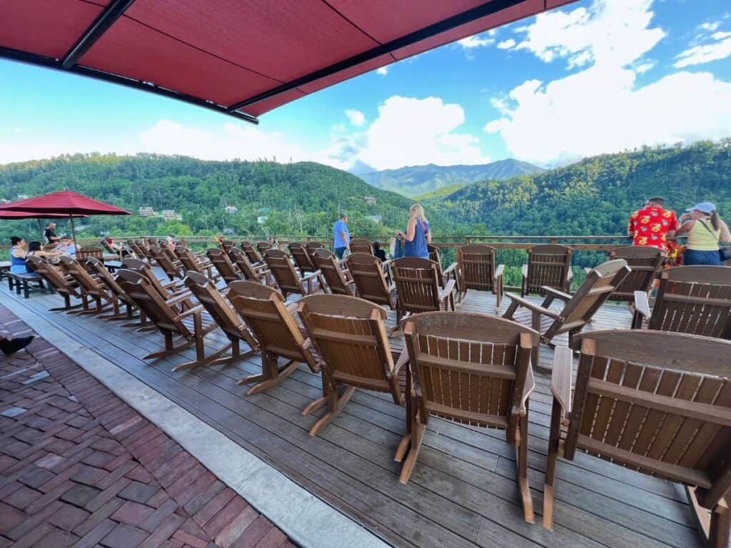 A woman strolls past lines of rocking chairs on a large deck with mountain views in Anakeesta.