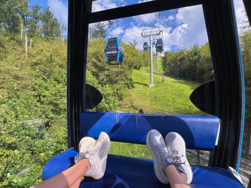 Two sets of feet sit on the seat on the opposite side of the gondola with a view up the mountain.